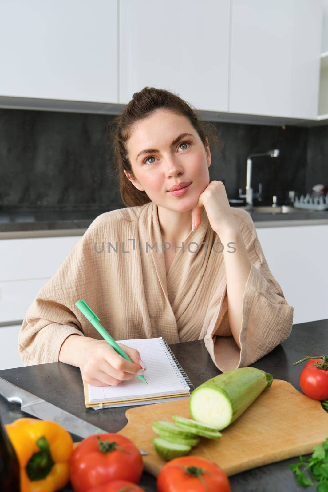 Portrait of woman sitting with groceries, making list for shopping, posing near vegetables, preparing food, cooking in the kitchen by Benzoix