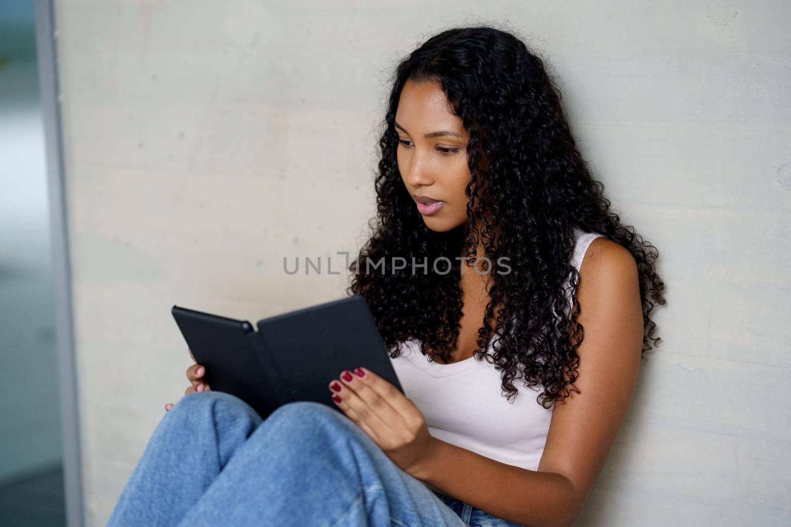 A young woman sits comfortably, fully engaged in her ebook, embodying the ideal themes of leisurely activities, the modern art of reading, and the role of technology in todays lifestyle