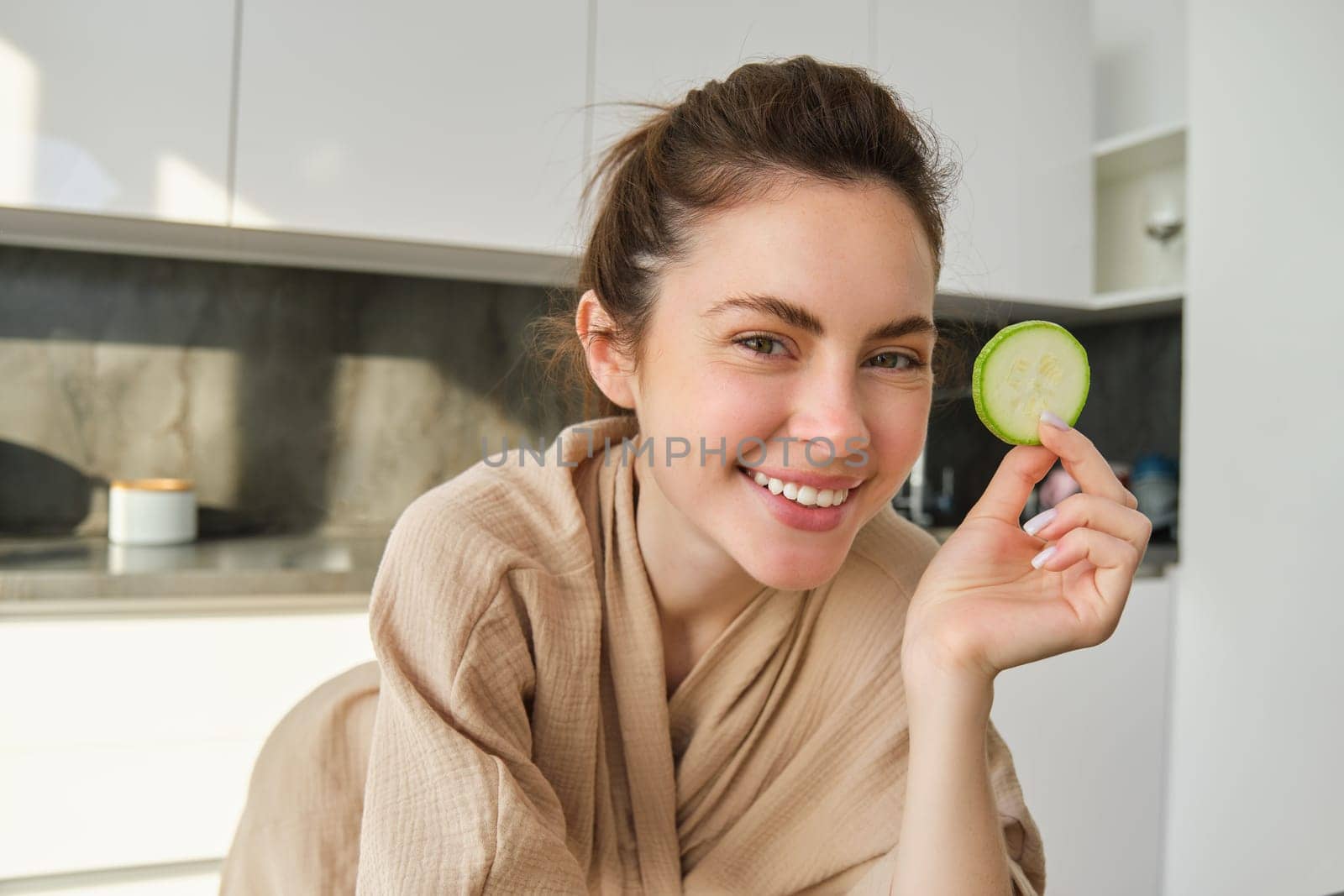 Portrait of happy, smiling young woman in the kitchen, cooking, chopping zucchini, holding vegetables and looking happy, preparing vegan food meal at home by Benzoix