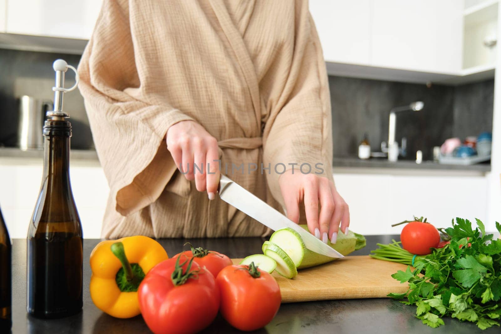 Healthy lifestyle. Young woman in bathrobe preparing food, chopping vegetables, cooking dinner on kitchen counter, standing over white background by Benzoix