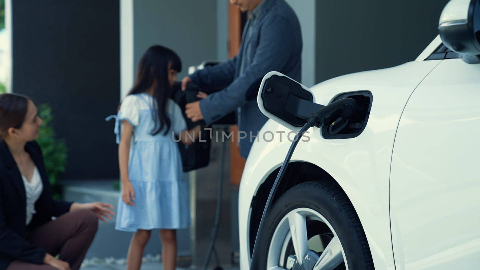 Progressive family with EV car and charging station prepare daughter to school. by biancoblue