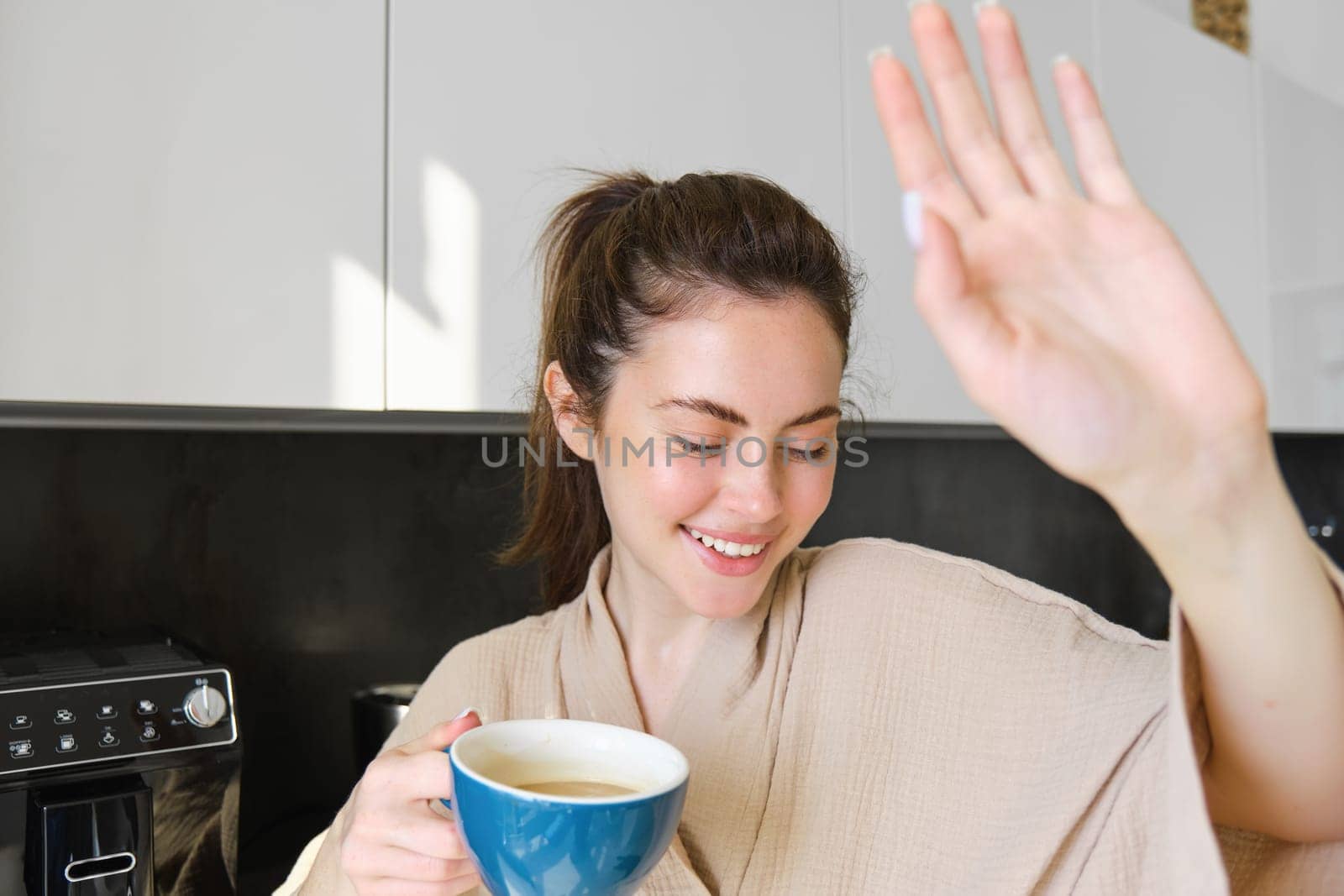 Portrait of beautiful girlfriend covers her face from camera and giggles, holding cup of coffee, concept of romantic mornings at home by Benzoix
