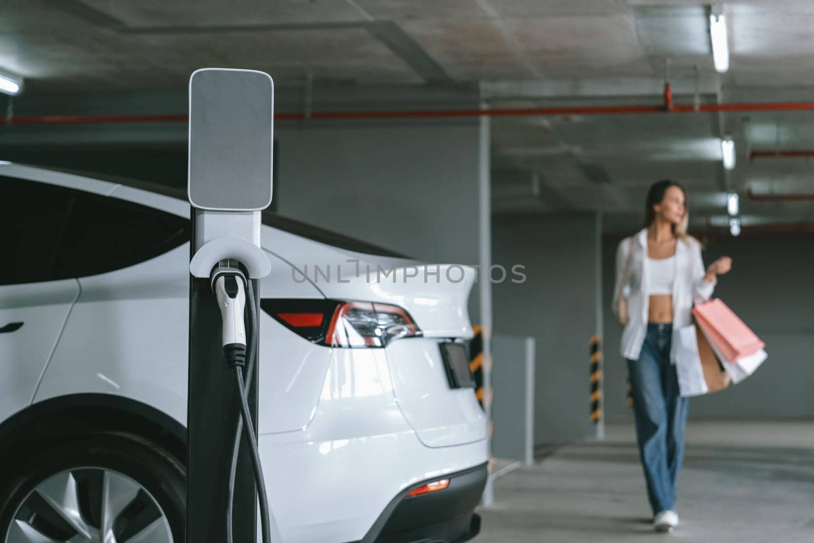 Young woman travel with EV electric car to shopping center parking lot innards by biancoblue