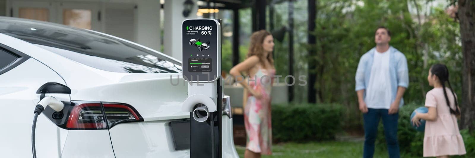 Focus EV station recharging battery for EV car on blurred family. Synchronos by biancoblue