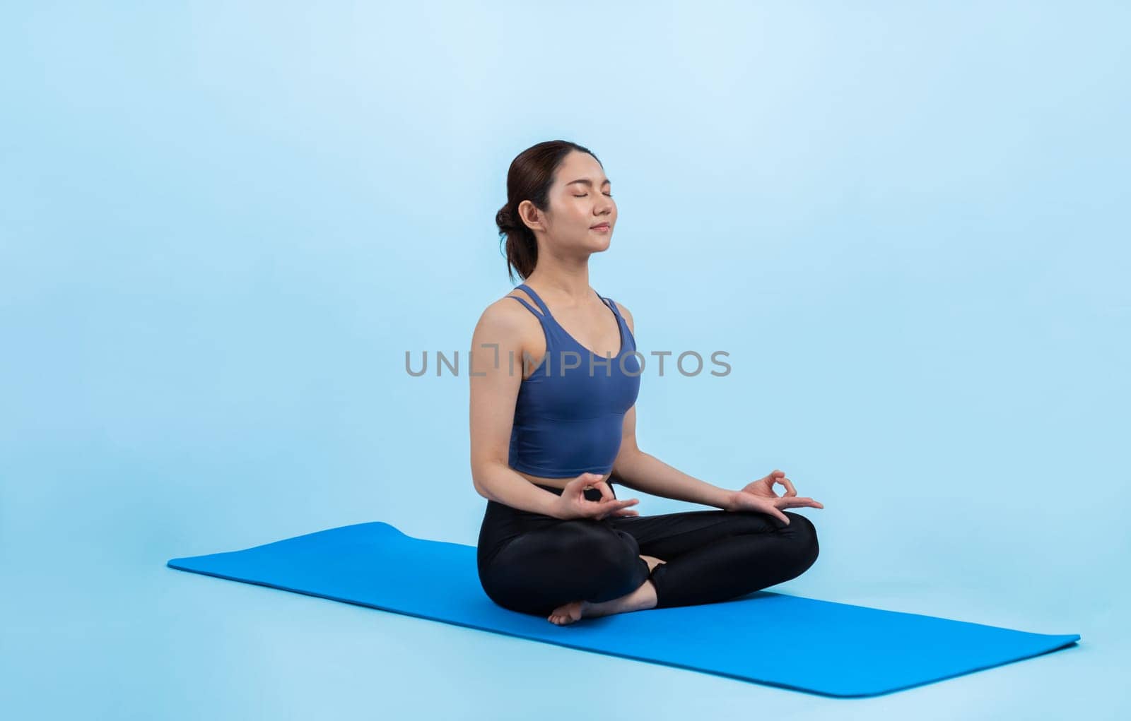 Asian woman in sportswear doing yoga exercise on fitness mat as her workout training routine. Healthy body care and calm meditation in yoga lifestyle in full body shot on isolated background. Vigorous