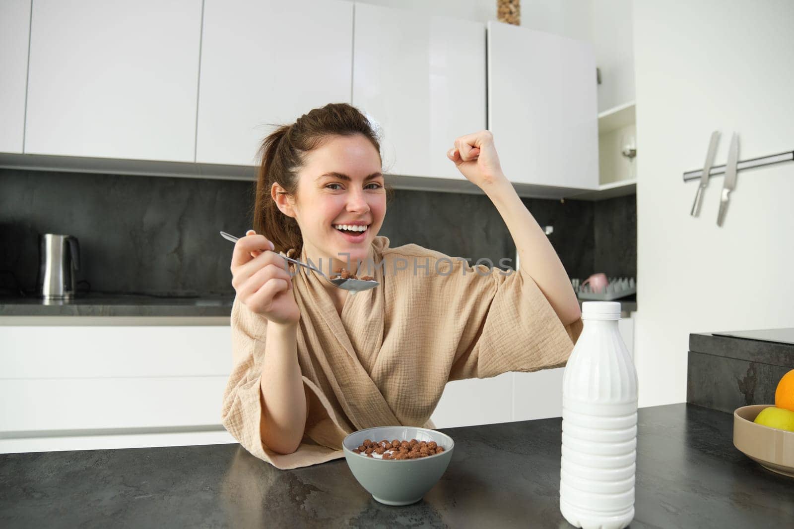 Portrait of happy, laughing young woman eating cereals with milk, triumphing, having breakfast and feeling excited, energetic morning concept by Benzoix