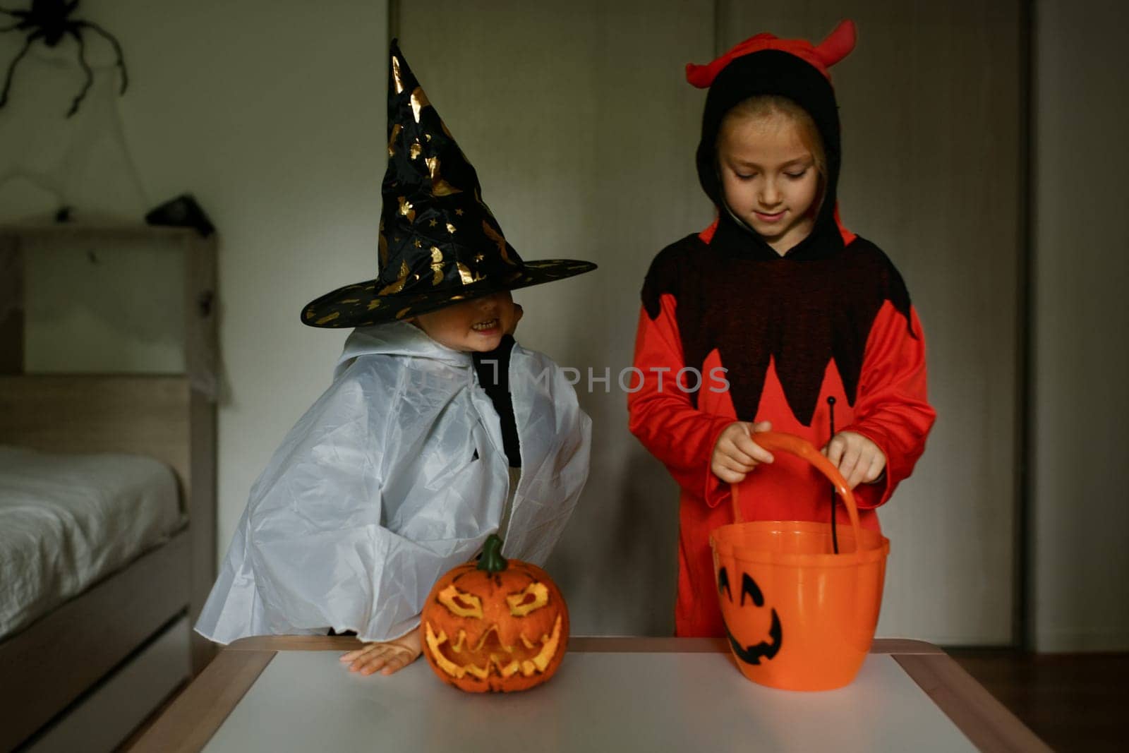 Children dressed as ghosts perform magic at home on Halloween by Godi