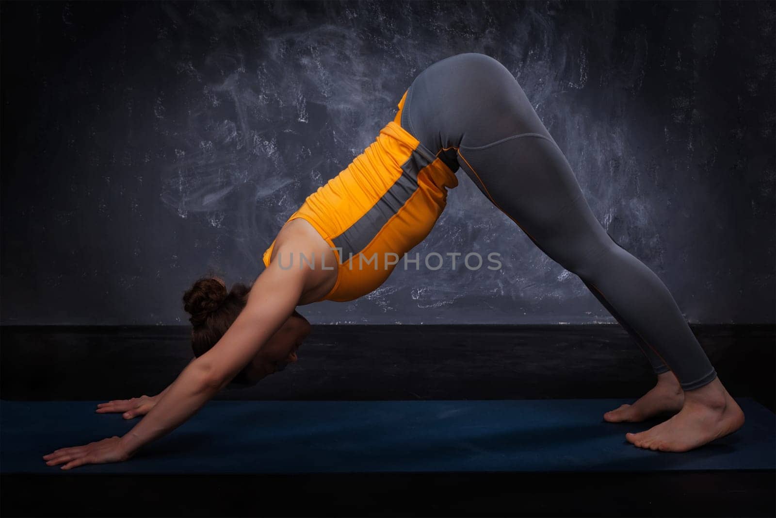 Beautiful sporty fit yogini woman practices yoga asana adhomukha svanasana - downward facing dog pose on dark background