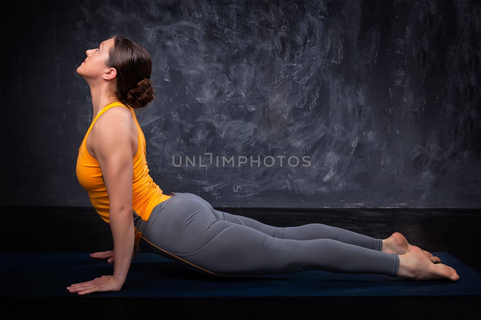 Beautiful sporty fit yogini woman practices yoga asana urdhva mukha svanasana - upward facing dog pose on dark background
