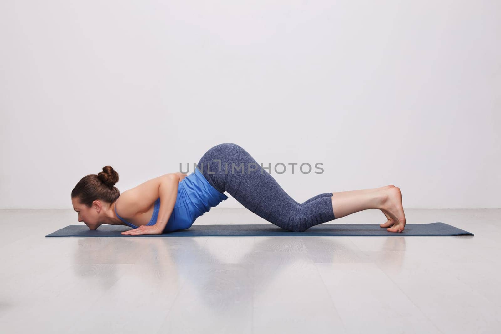 Beautiful sporty fit yogini woman practices yoga asana Ashtangasana - eight-limbed pose variation in studio