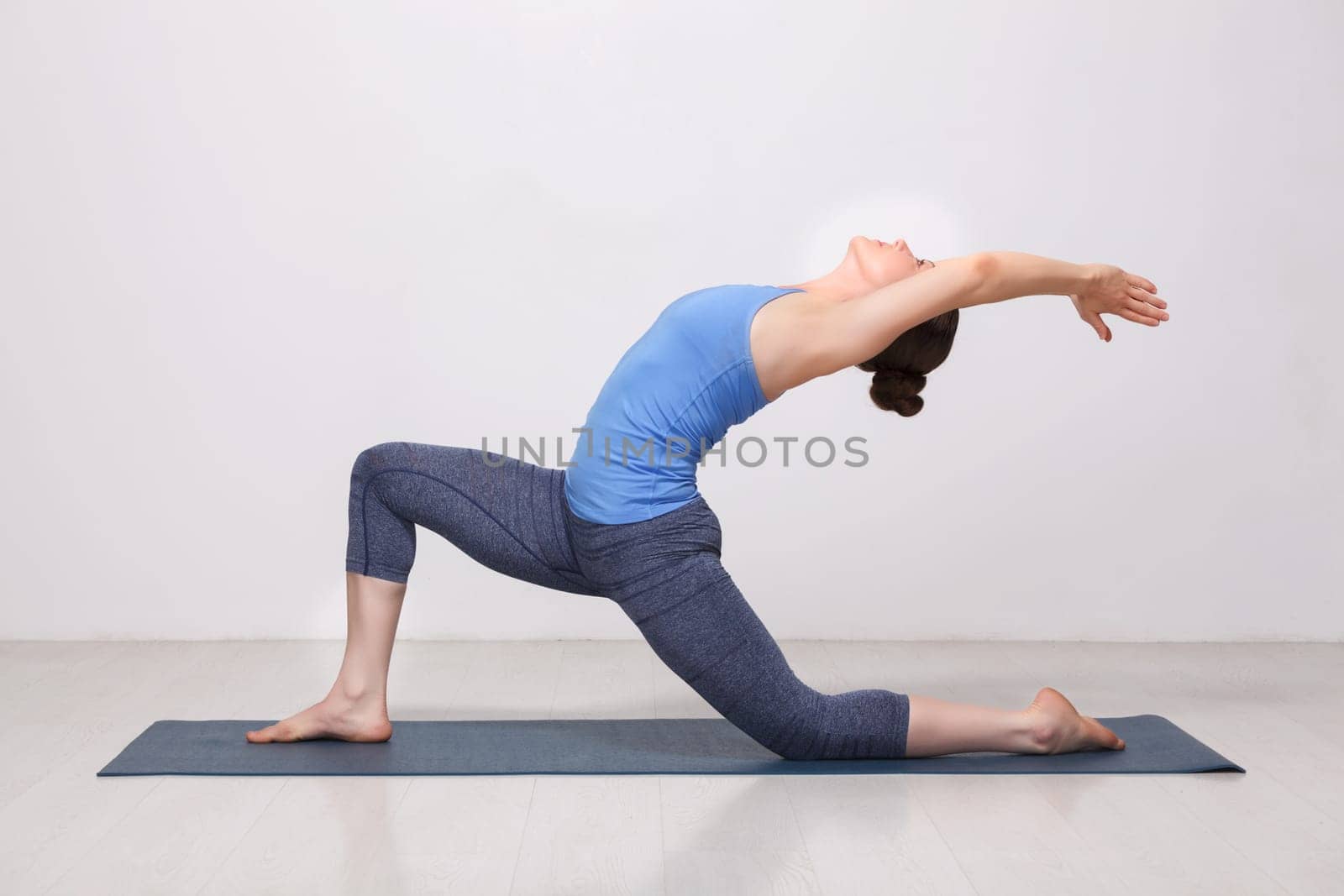 Beautiful sporty fit yogini woman practices yoga asana Anjaneyasana - low crescent lunge pose in surya namaskar in studio