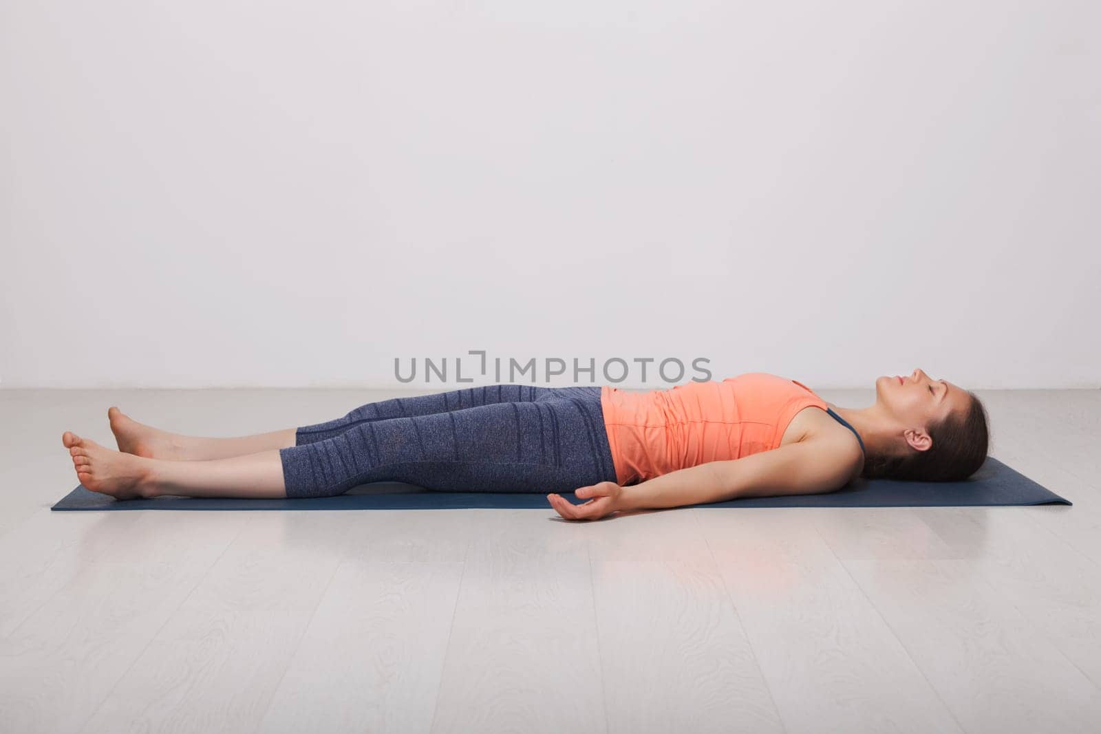 Beautiful sporty fit yogini woman relaxes in yoga asana Savasana - corpse pose in studio