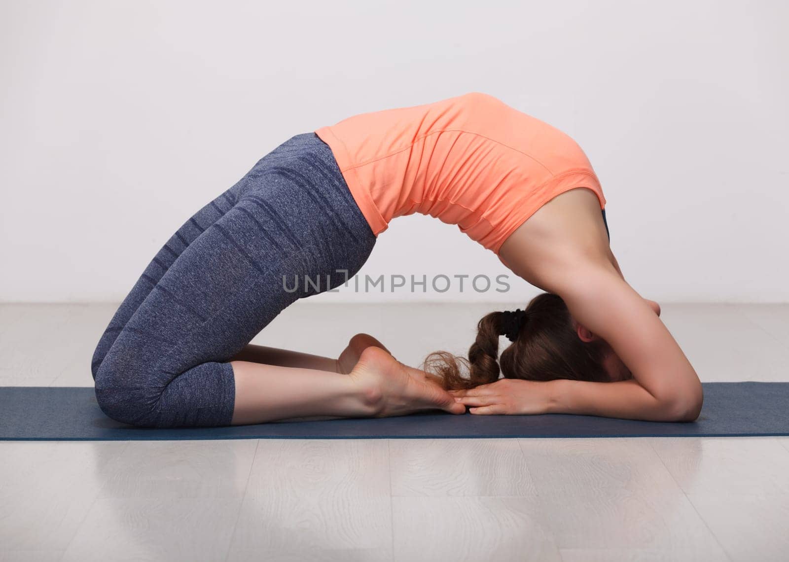 Beautiful sporty fit yogini woman practices yoga asana Kapotasana - pigeon pose intense backbend in studio