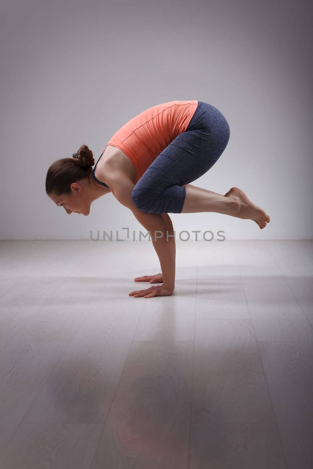 Beautiful sporty fit yogini woman practices yoga asana kakasana - crow pose in studio