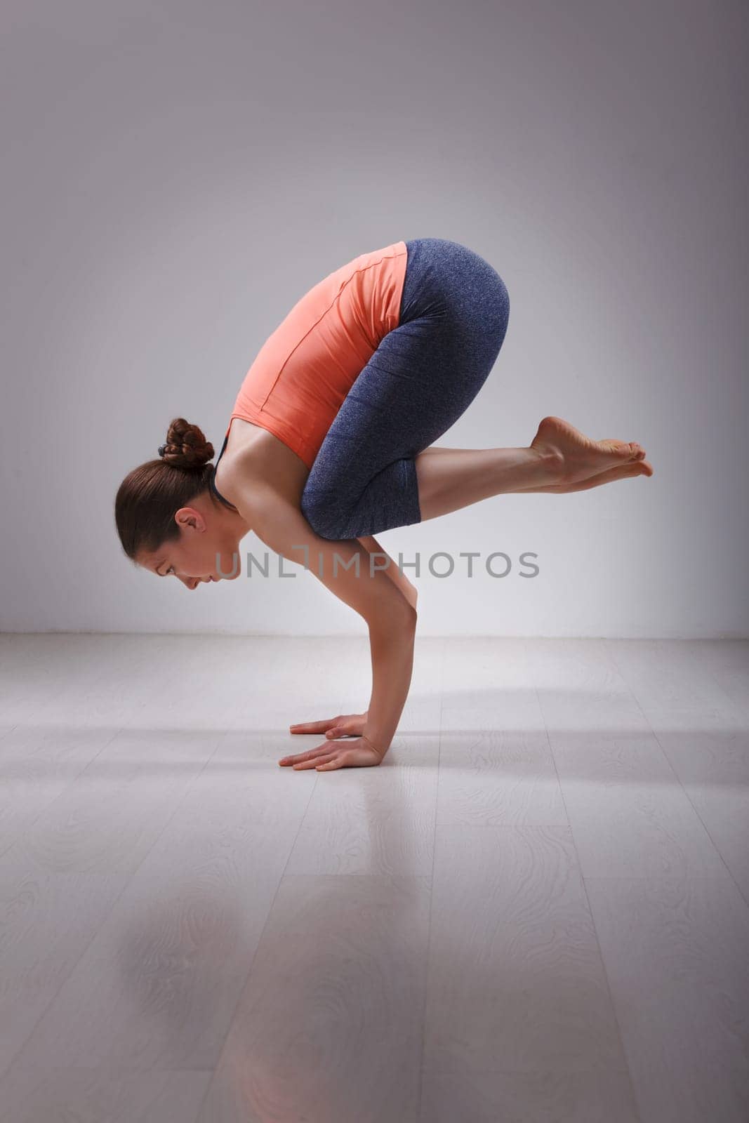 Beautiful sporty fit yogini woman practices yoga asana Bakasana - crane pose arm balance in studio