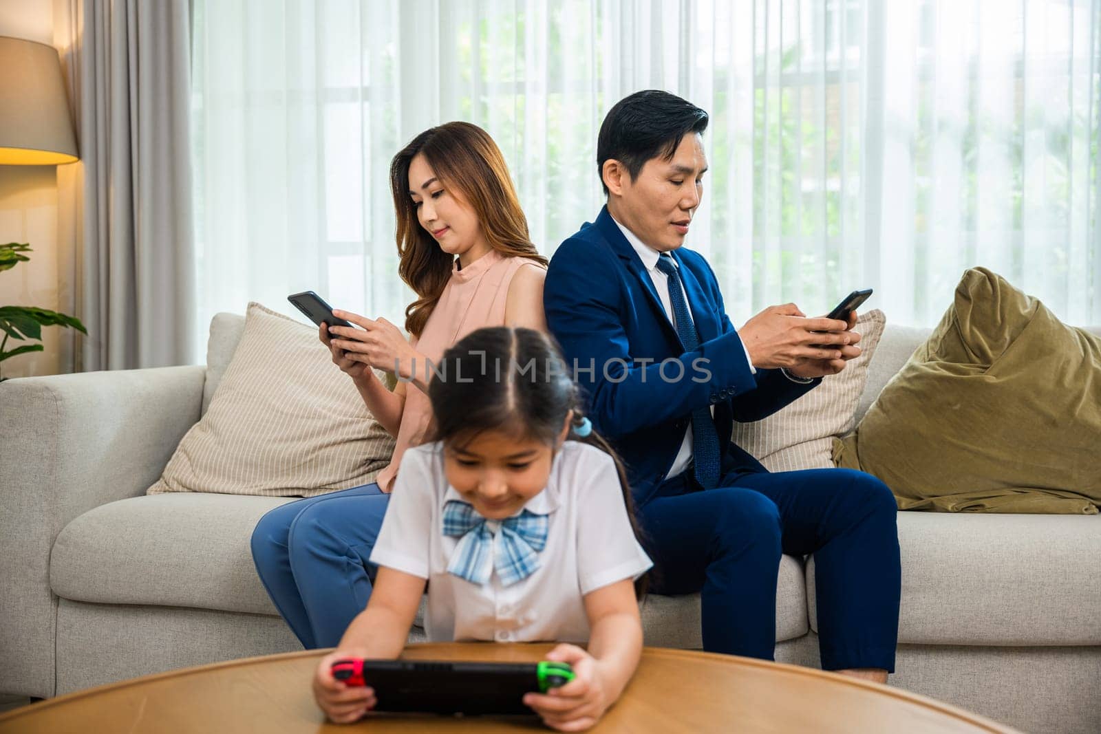 Asian parents ignore their child and looking at their mobile phone at home by Sorapop