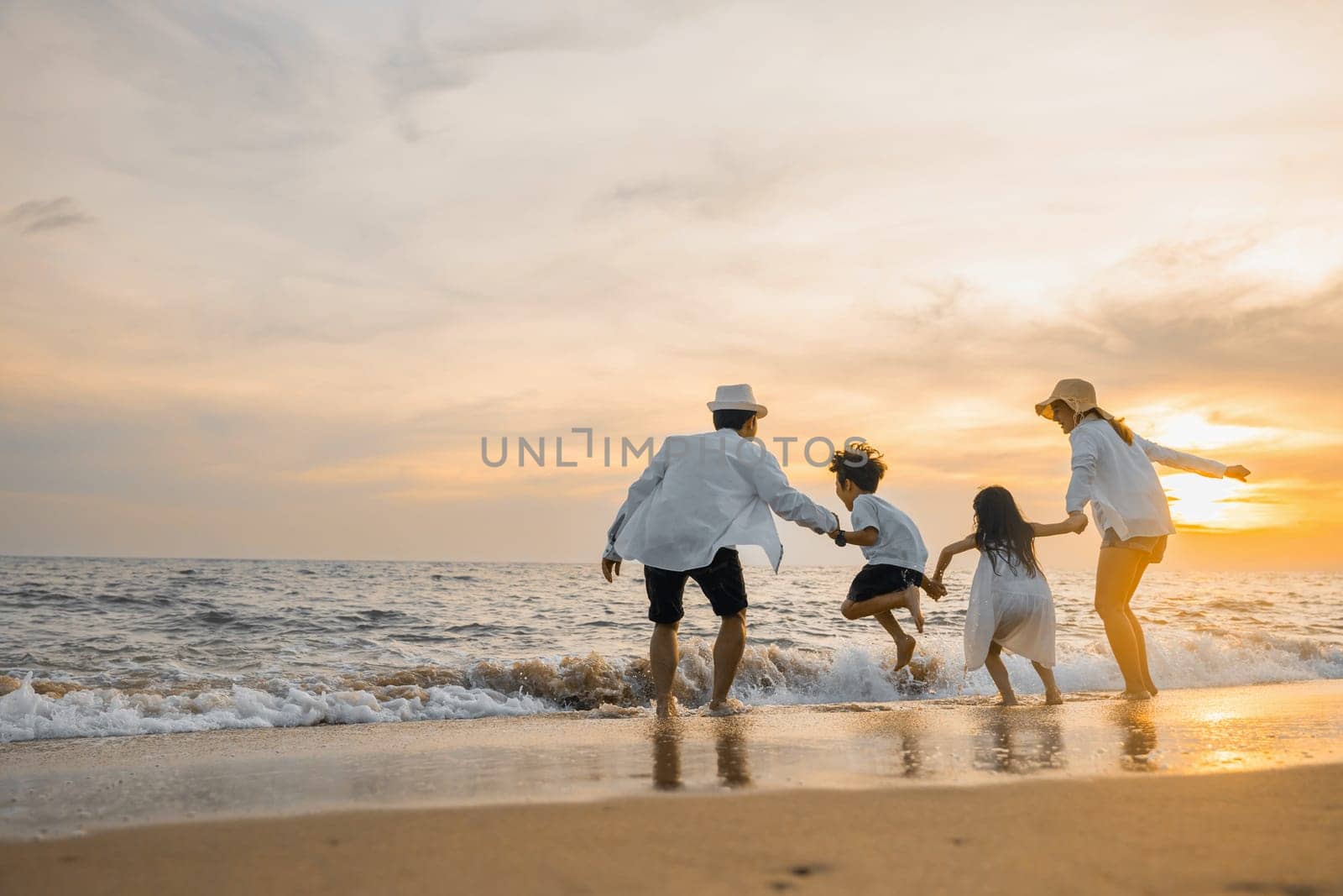 Happy family have fun jumping on beach in holiday at sunset, Back people enjoying travel trip and vacations, Silhouette of family father, mother, son and daughter holding hands jump together on beach