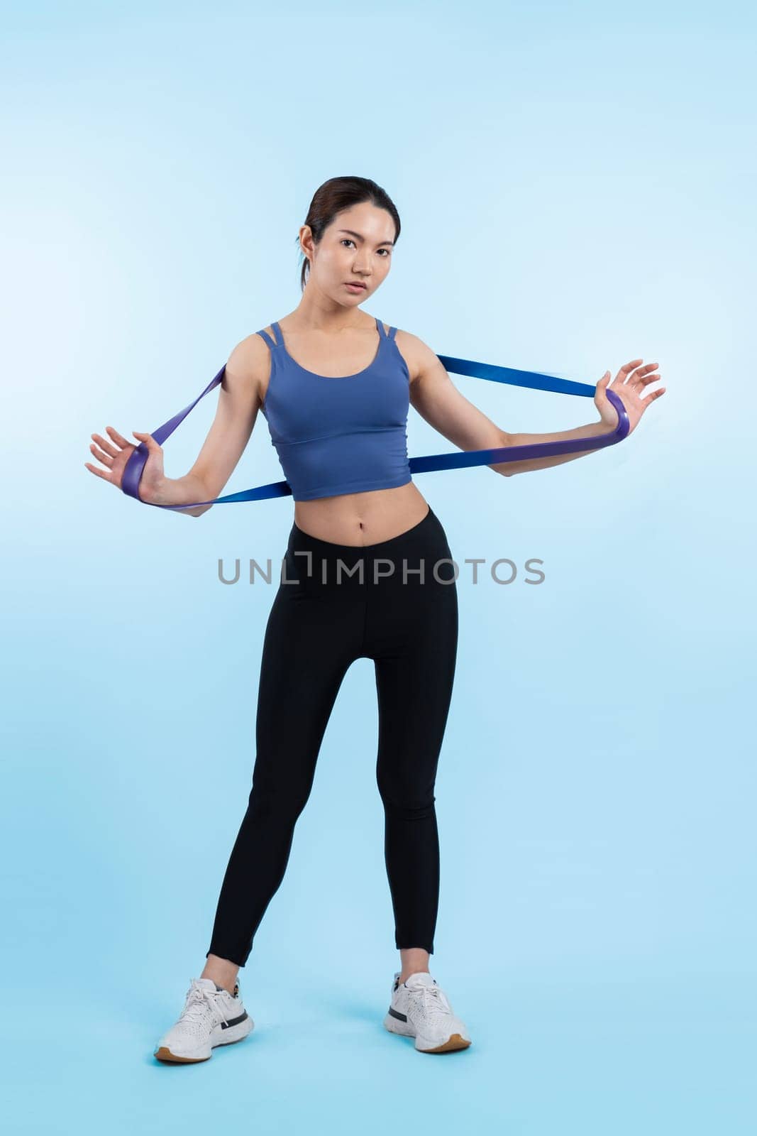 Vigorous energetic woman in sportswear portrait stretching resistance sport band. Young athletic asian woman strength and endurance training session workout routine concept on isolated background.