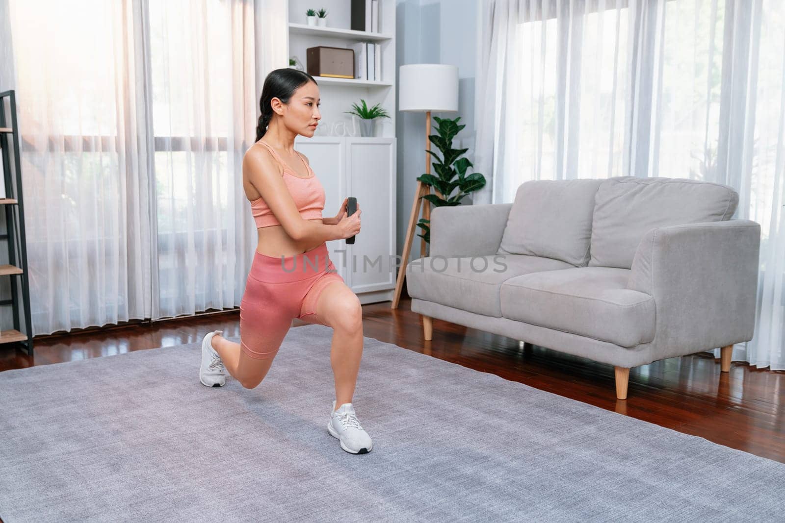 Vigorous energetic woman doing yoga and weight lifting exercise at home. Young athletic asian woman strength and endurance training session as home workout routine.