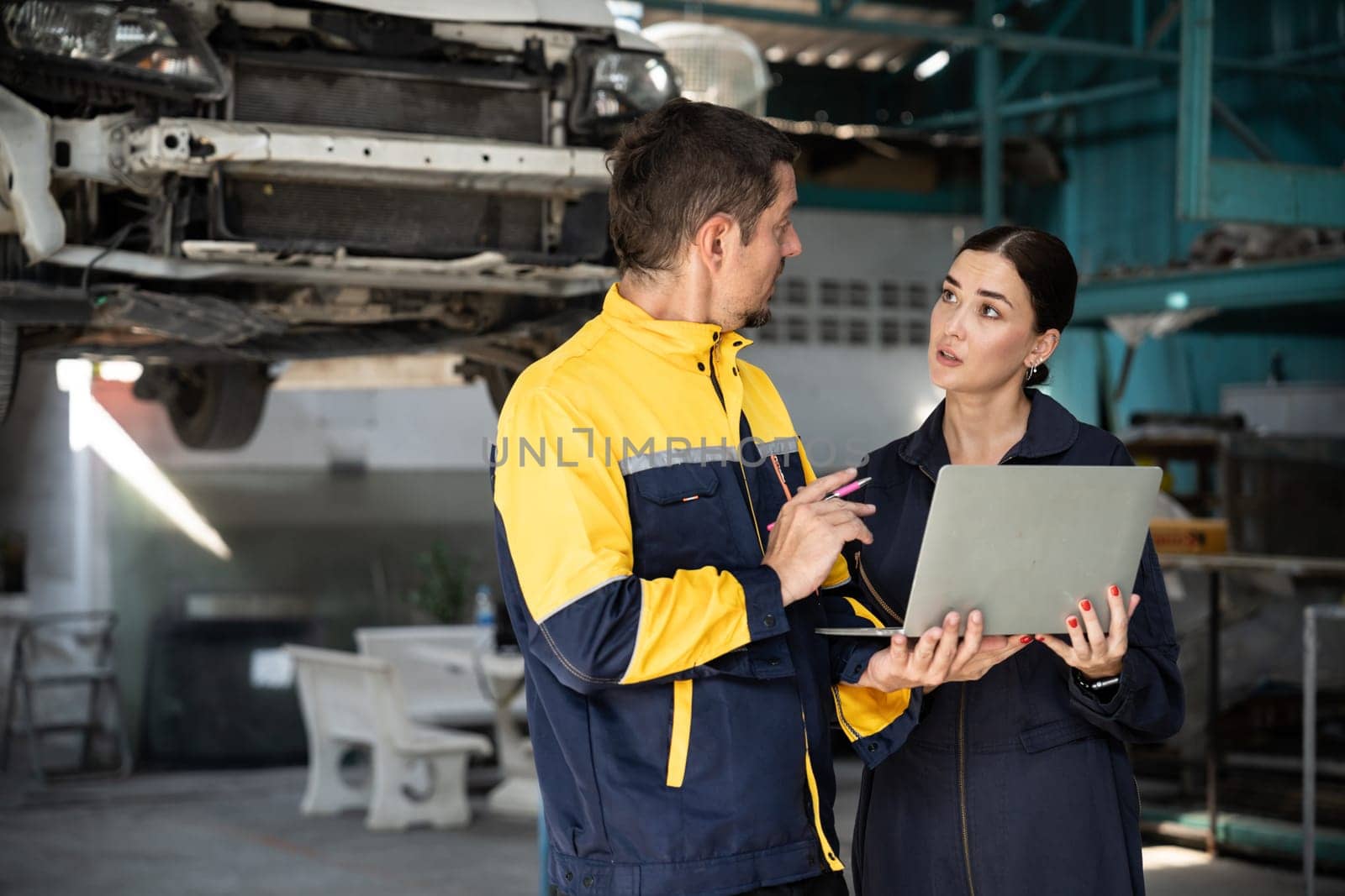 Two vehicle mechanic working together, conduct car inspection with laptop. Automotive service technician in uniform carefully make diagnostic troubleshooting to identify error. oxus