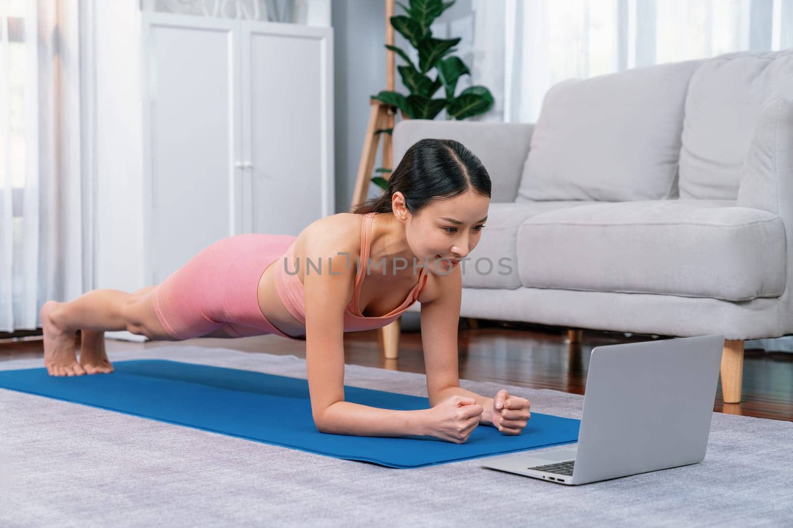 Fit young asian woman planing on the living room floor while following exercise instruction on online training video. Healthy lifestyle workout routine at home. Balance and endurance concept. Vigorous