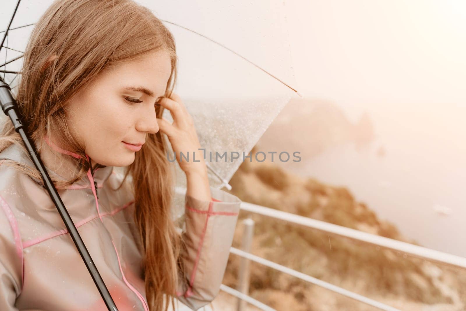 Woman rain park. Happy woman portrait wearing a raincoat with transparent umbrella outdoors on rainy day in park near sea. Girl on the nature on rainy overcast day