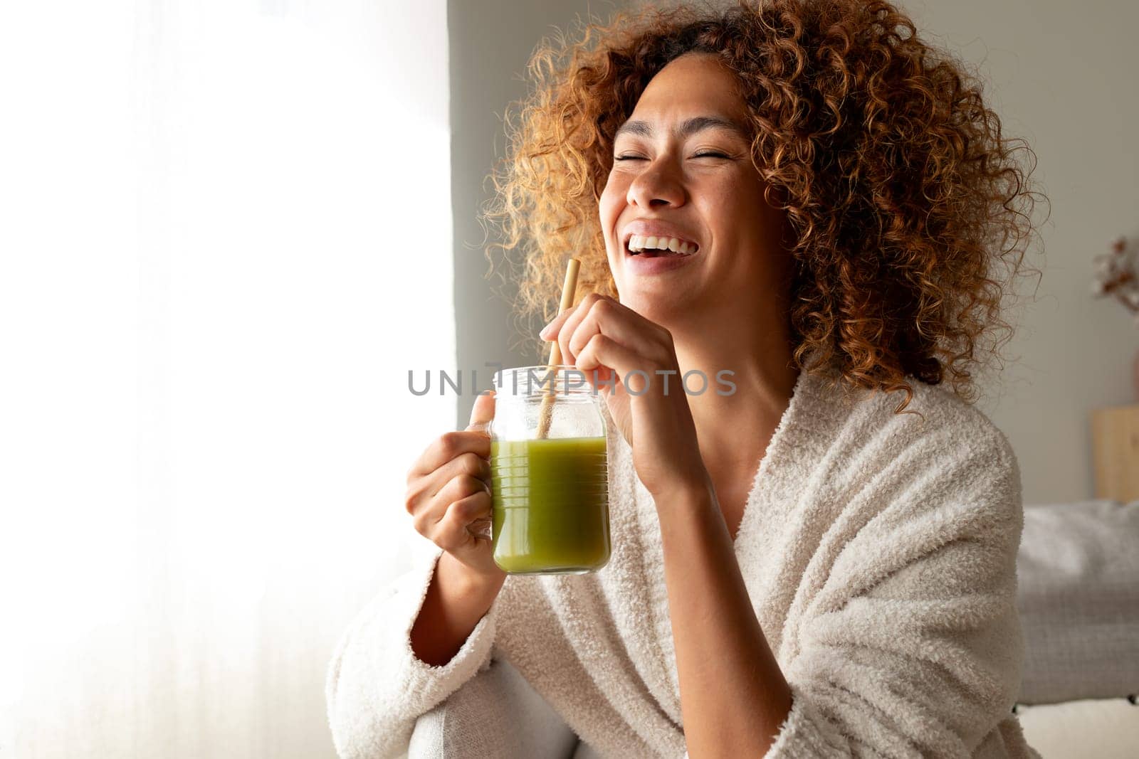 Happy multiracial woman enjoying healthy green juice at home. Female doing detox drinking green smoothie. Copy space. by Hoverstock