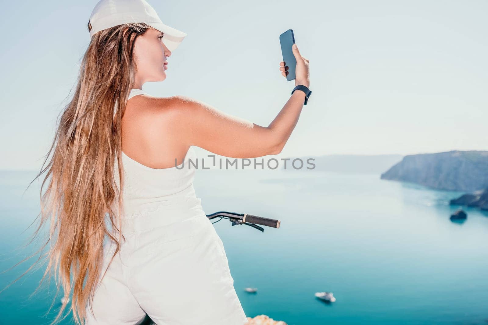 A woman cyclist on a mountain bike looking at the landscape of mountains and sea. Rear view of cyclist woman standing in front to the sea with outstretched arms. Freedom and healthy lifestyle concept. by panophotograph