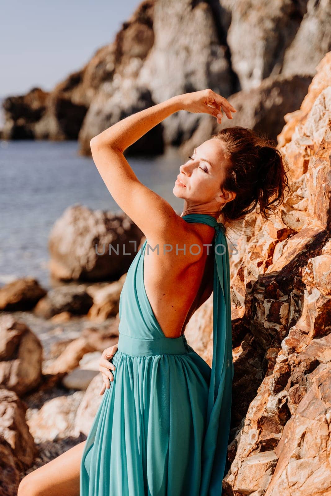 Woman green dress sea. Woman in a long mint dress posing on a beach with rocks on sunny day. Girl on the nature on blue sky background. by Matiunina