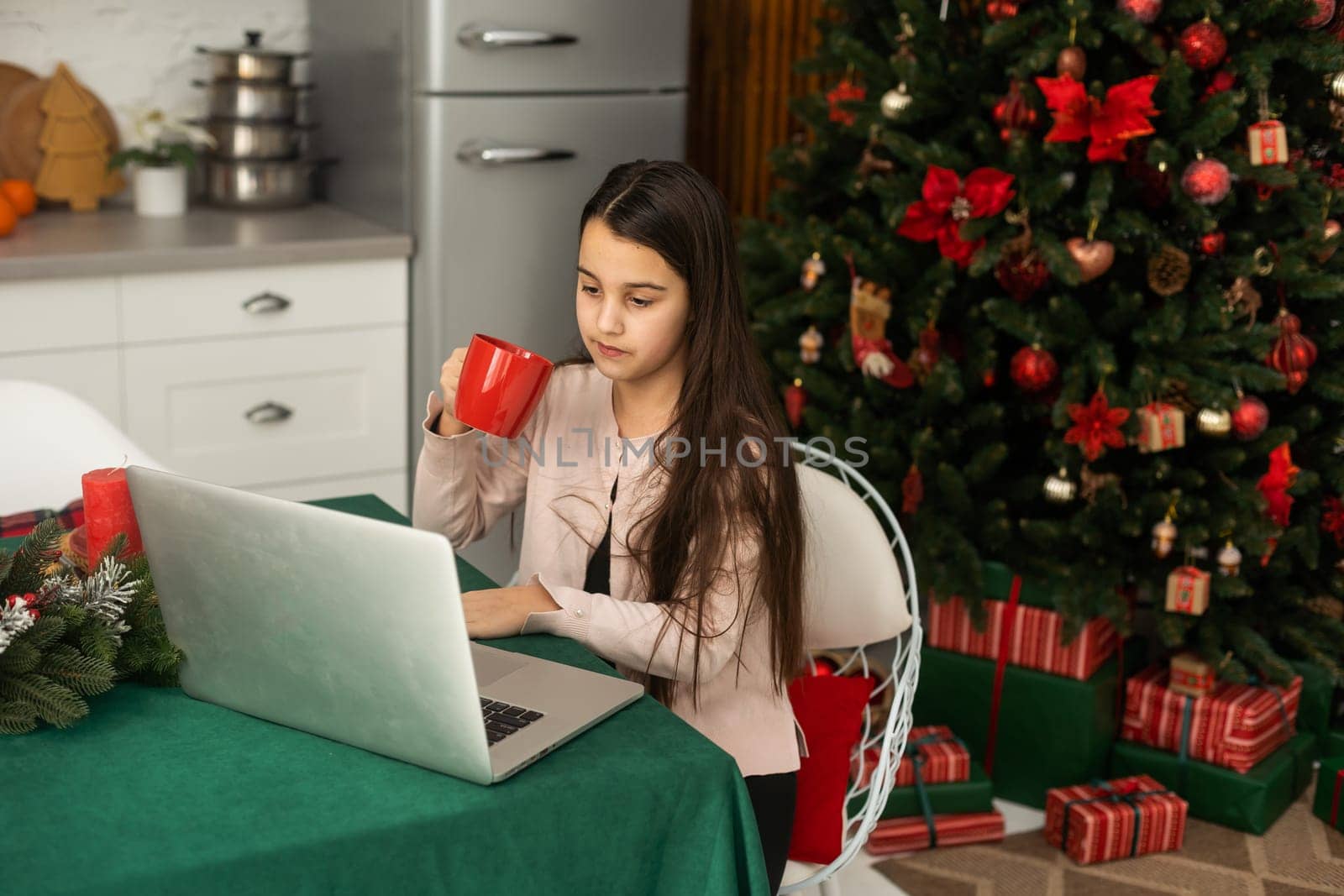 Teenage girl with gifts and laptop near the Christmas tree. Living room interior with Christmas tree and decorations. New Year. Gift giving