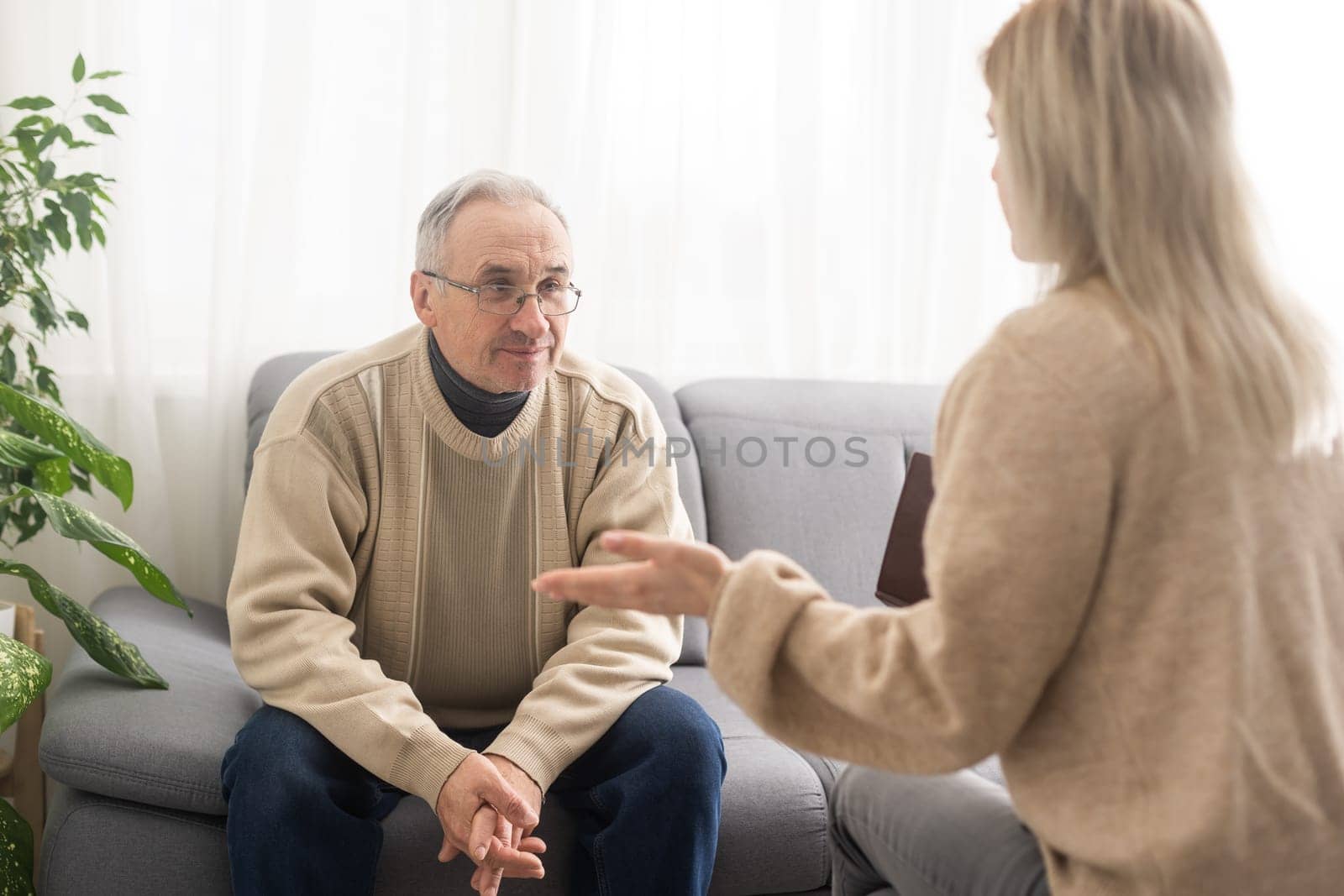 Senior man patient and young woman caregiver medical worker in uniform hold clipboard noting personal information talking listens client telling about health complaints, care support nursing concept