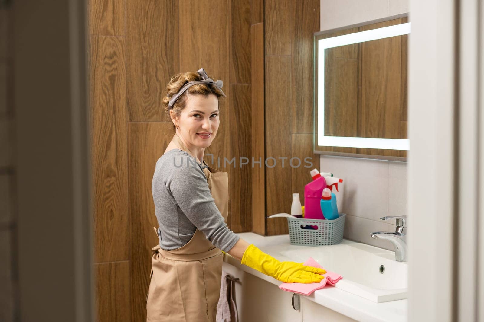 Young woman doing house chores. Woman holding cleaning tools. Woman wearing rubber protective yellow gloves, holding rag and spray bottle detergent. It's never too late to spring clean.