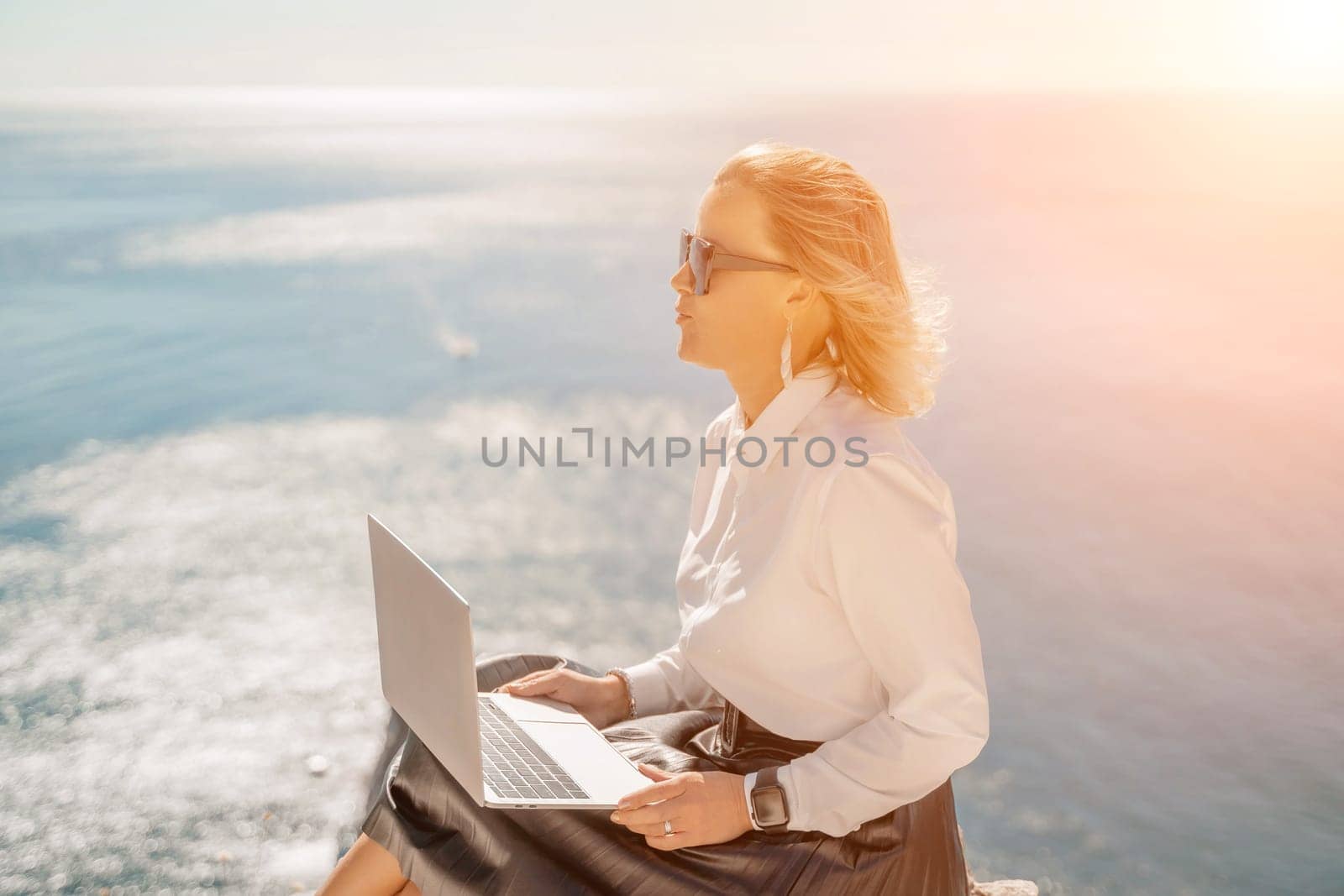 Business woman on nature in white shirt and black skirt. She works with an iPad in the open air with a beautiful view of the sea. The concept of remote work