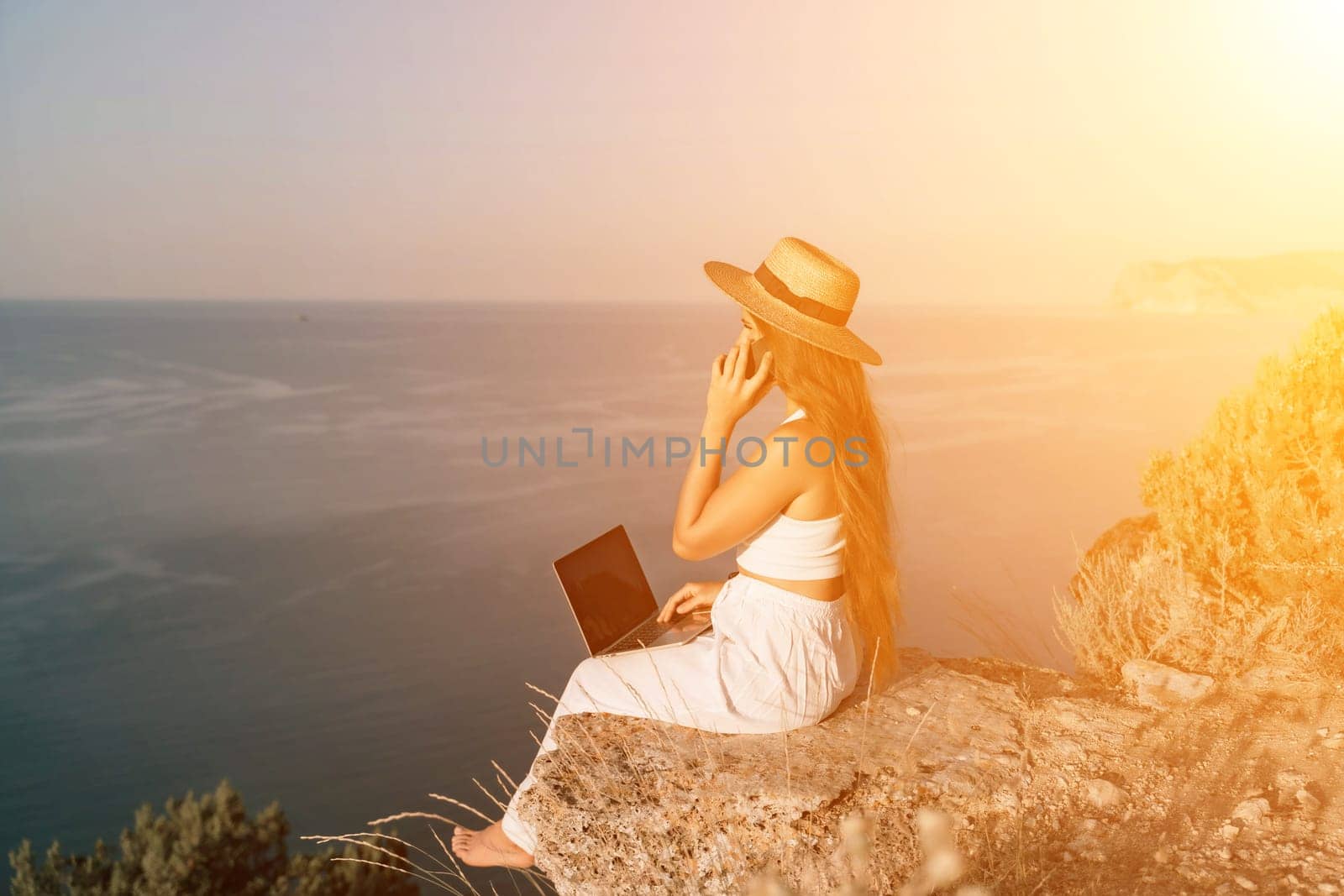 Freelance happy woman typing on her laptop, enjoying the picturesque sea view, highlighting the idea of working remotely with a relaxed and pleasant atmosphere