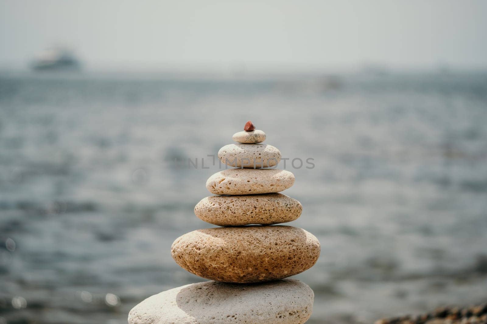 Balanced rock pyramid on sea pebbles beach, at sunset. Golden sea bokeh on background. Selective focus, zen stones on sea beach, meditation, spa, harmony, calm, balance concept by panophotograph