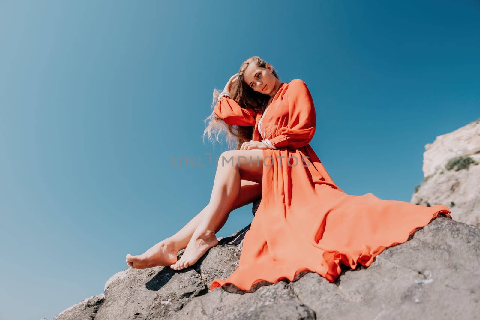 Woman travel sea. Young Happy woman in a long red dress posing on a beach near the sea on background of volcanic rocks, like in Iceland, sharing travel adventure journey by panophotograph