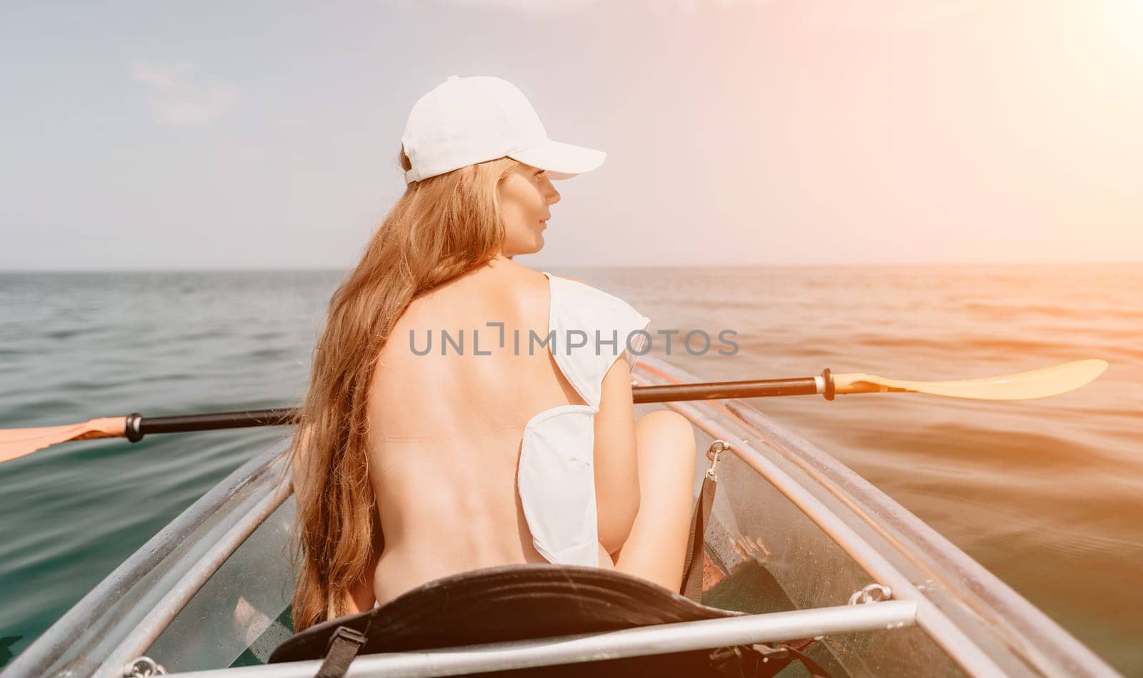 Woman in kayak back view. Happy young woman with long hair floating in transparent kayak on the crystal clear sea. Summer holiday vacation and cheerful female people relaxing having fun on the boat by panophotograph