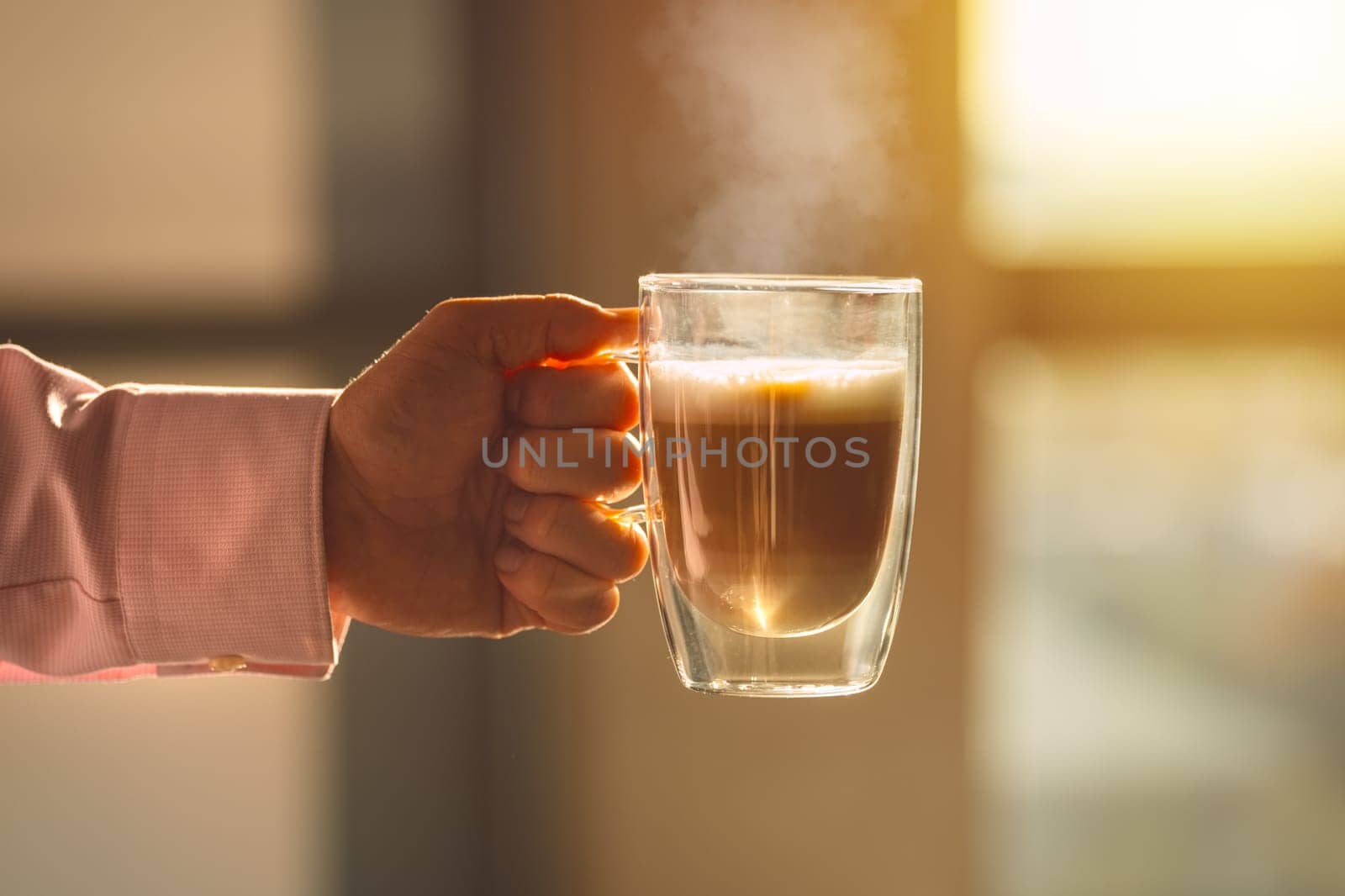 A cozy photo of a hand holding a steaming cup of coffee. The photo invokes warm feelings associated with sipping hot drinks before working day. High quality photo