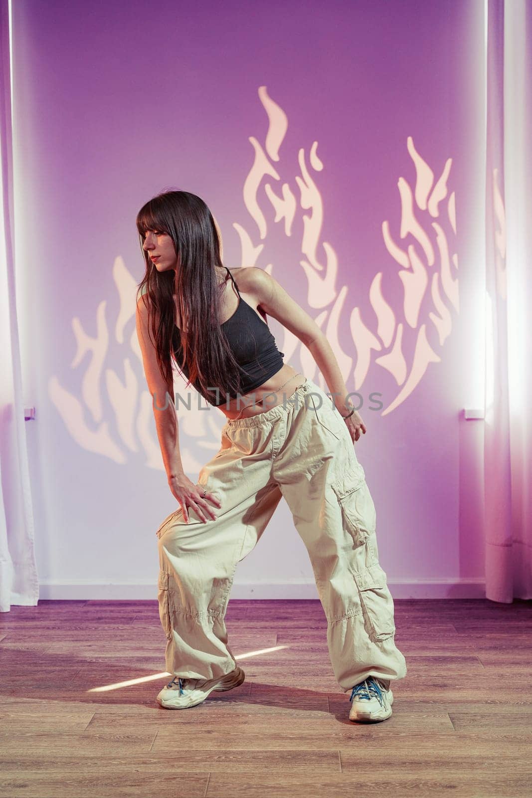 A dancer gracefully performs in a studio illuminated by dramatic lighting. The vibrant flame-inspired backdrop adds energy to the creative expression, highlighting her fluidity and style.