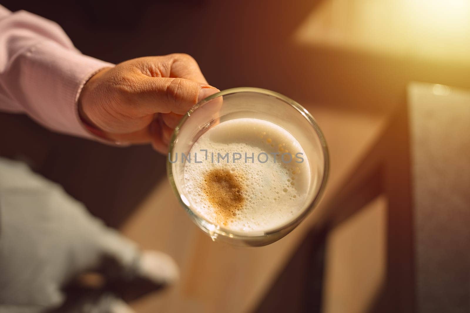 A cozy photo of a hand holding a cup of cappuccino coffee. The photo invokes warm feelings associated with sipping hot drinks before working day. High quality photo