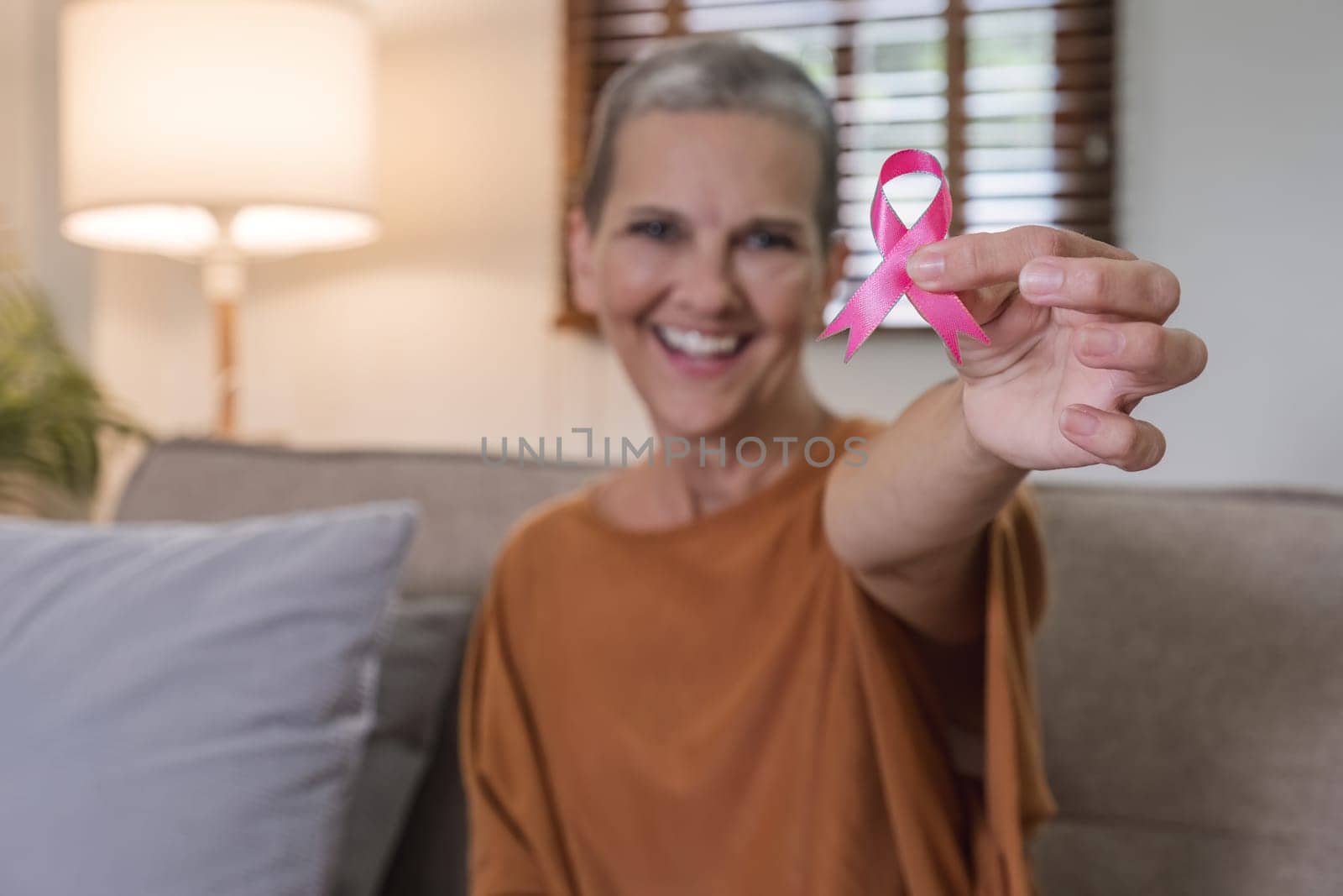 Portrait of confident smiling elderly senior woman with pink ribbon at her home. Health care, support, prevention. Breast cancer awareness month concept.