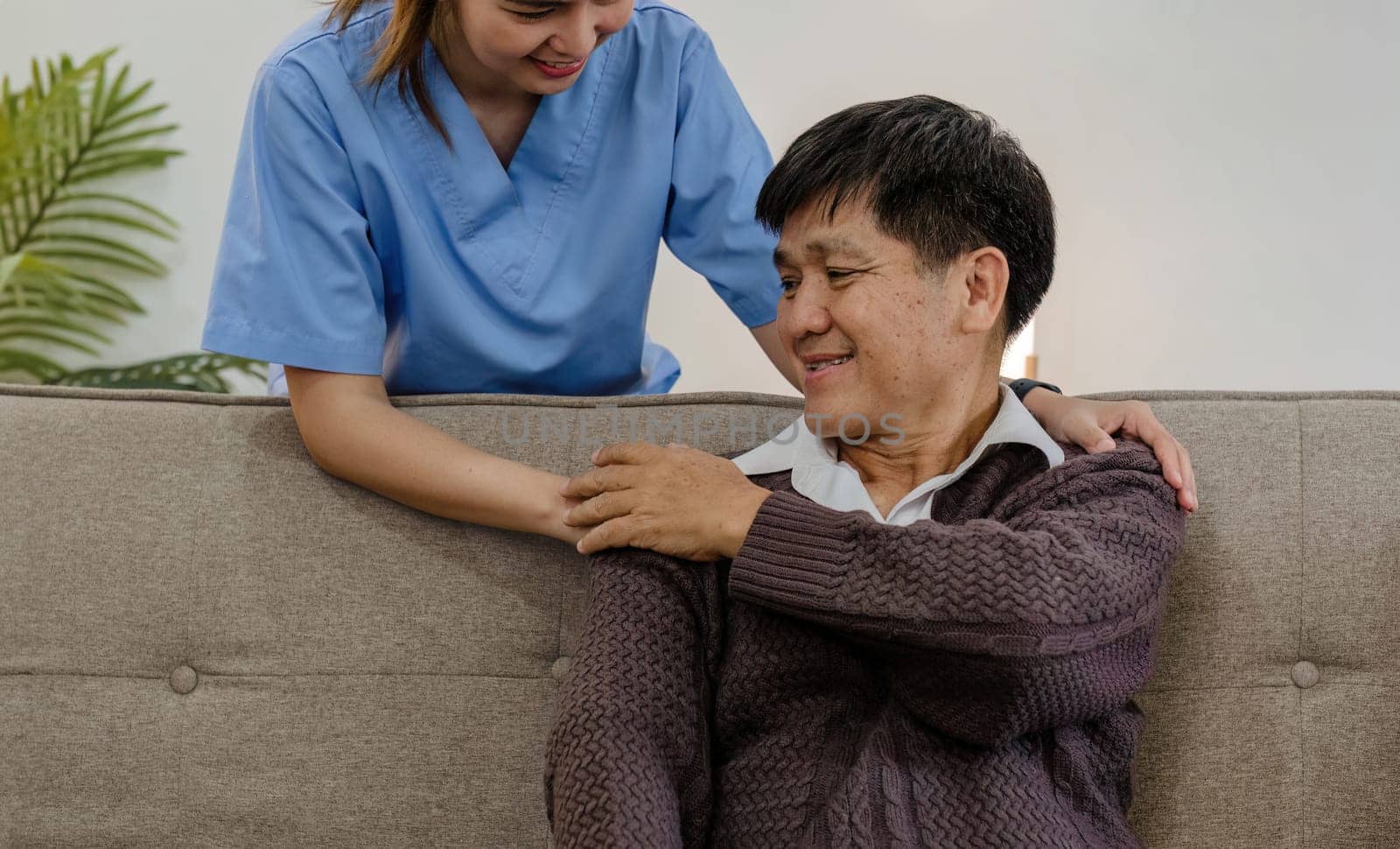 Nurse supports man during recovery A caregiver holds the hand of a senior patient who is resting in the living room and shows kindness while checking up on a retired person at home. by wichayada