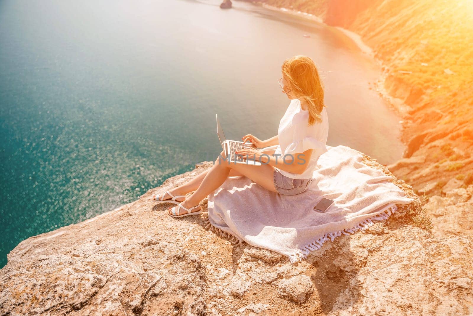 Freelance woman working on a laptop by the sea, typing away on the keyboard while enjoying the beautiful view, highlighting the idea of remote work. by Matiunina