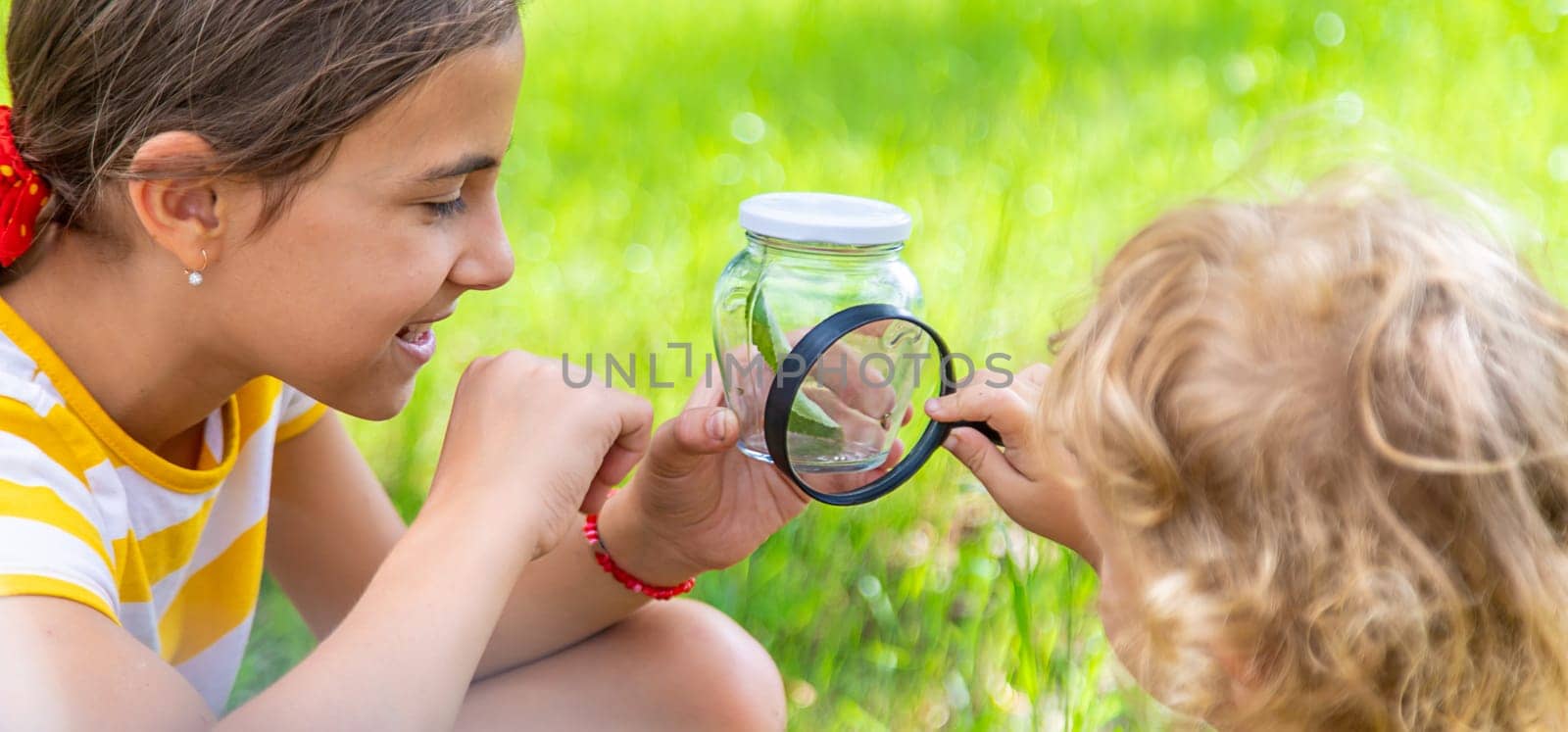 A child studies a beetle in a jar with a magnifying glass. Selective focus. Nature.