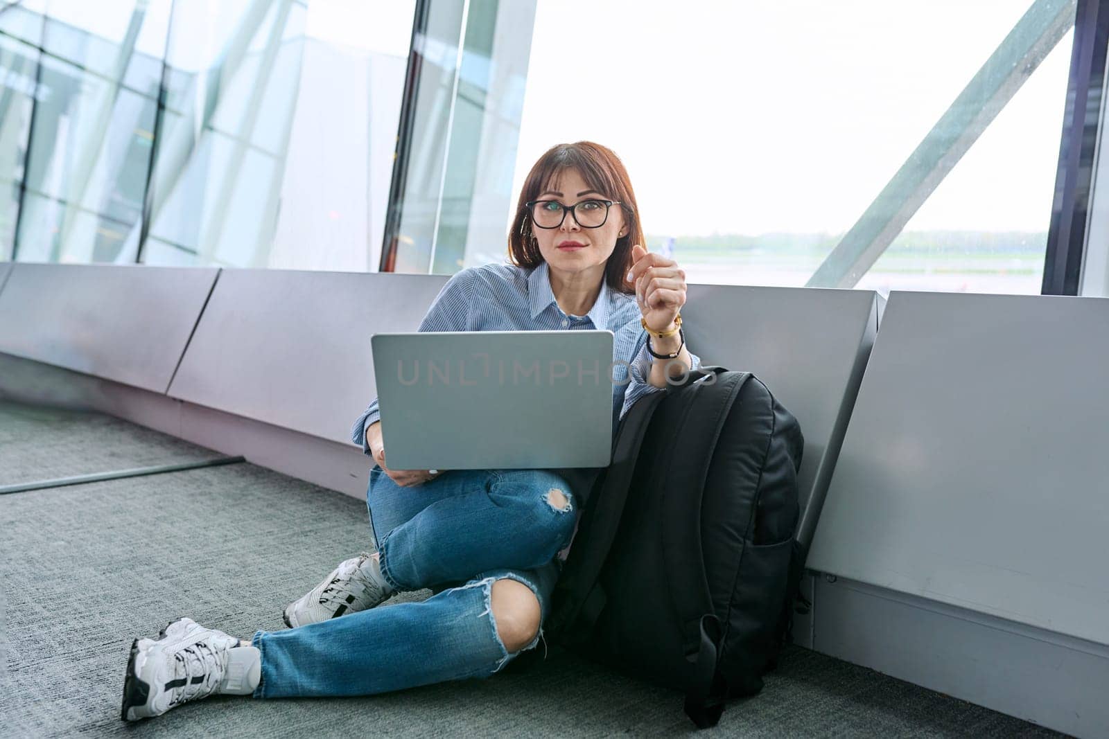 Woman waiting for airplane flight in airport terminal, using laptop by VH-studio