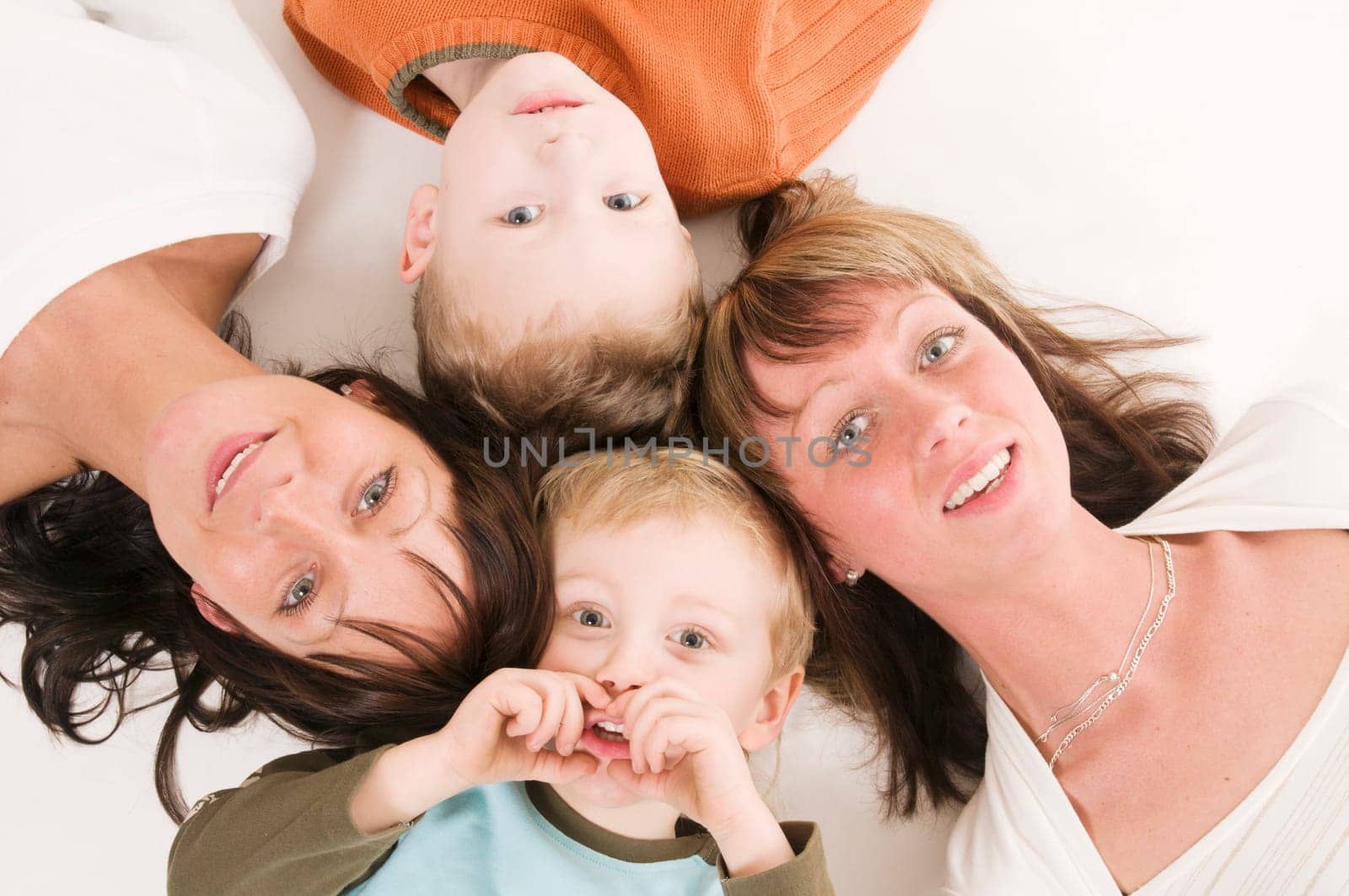 two adult sisters with their sons lie on their backs and look at the camera