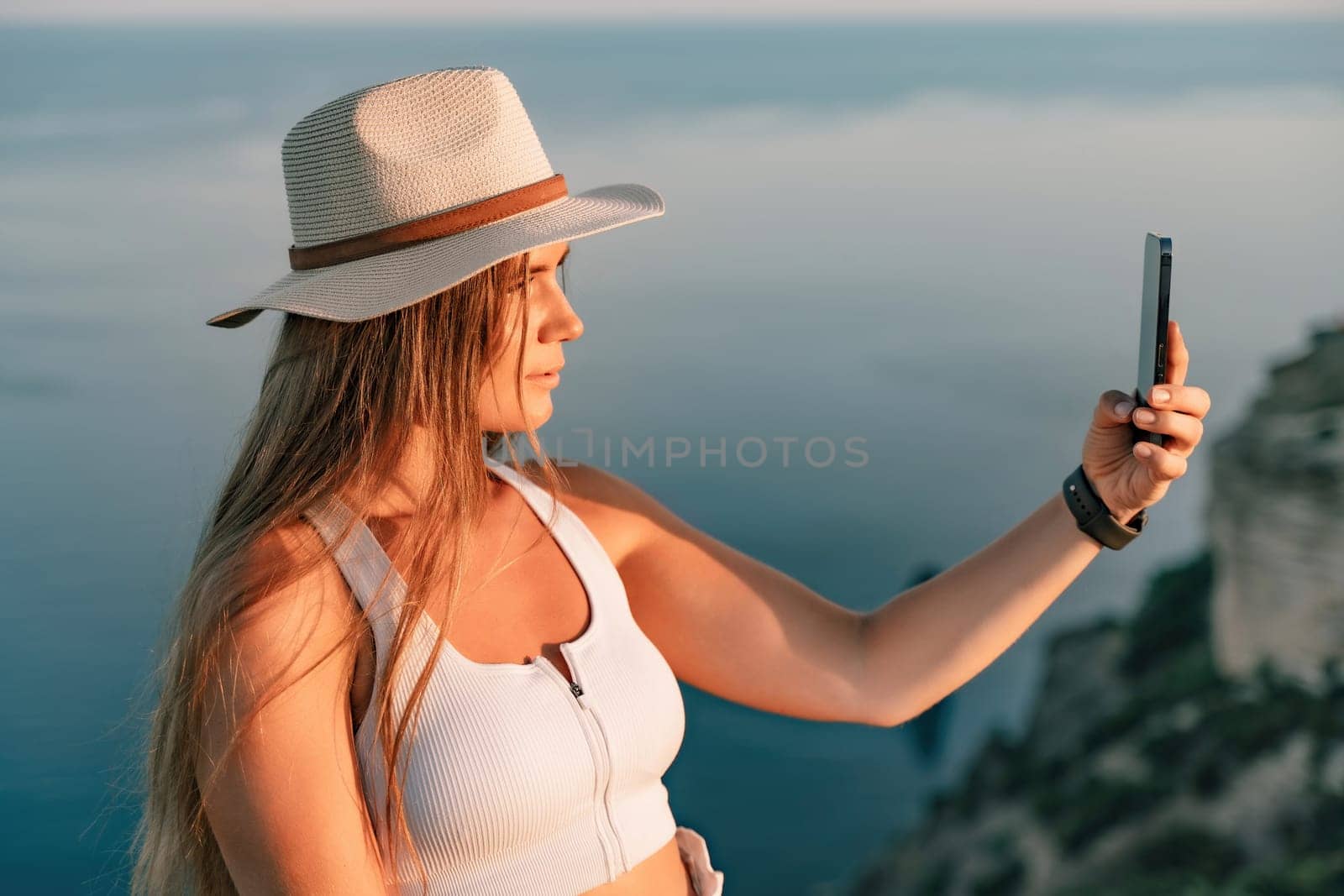 Selfie woman in hat, white tank top and shorts makes selfie shot mobile phone post photo social network outdoors on sea background beach people vacation lifestyle travel concept. by Matiunina