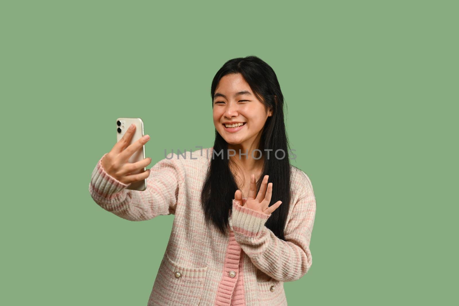 Cheerful teenage girl with smartphone standing on green background. People, technology and communication. by prathanchorruangsak