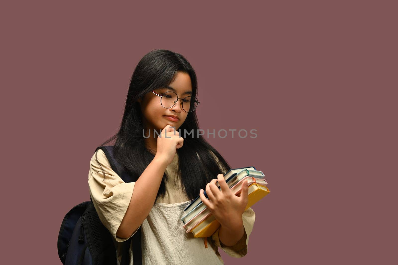 Teenager schoolgirl wearing glasses holding textbook over purple background. Educational, learning and back to school concept by prathanchorruangsak