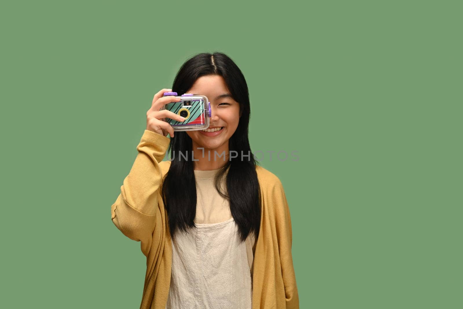 Happy Asian teenage girl with film camera posing isolated on green background by prathanchorruangsak